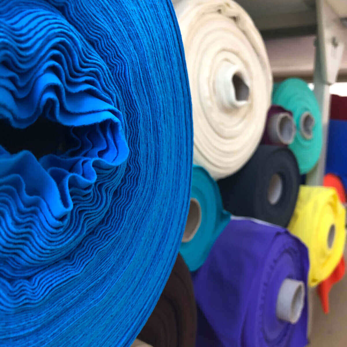 Rolls of colorful fabrics for pole dance clothing, featuring vibrant shades like blue and purple, ideal for stylish pole wear.